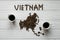 Map of the Vietnam made of roasted coffee beans laying on white wooden textured background with two cups of coffee