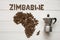 Map of the Zimbabwe made of roasted coffee beans laying on white wooden textured background with coffee maker