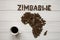 Map of the Zimbabwe made of roasted coffee beans laying on white wooden textured background with cup of coffee