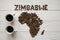 Map of the Zimbabwe made of roasted coffee beans laying on white wooden textured background with two cups of coffee