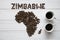 Map of the Zimbabwe made of roasted coffee beans laying on white wooden textured background with two cups of coffee