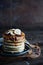 Maple syrup pouring onto a stack of pancakes against dark background