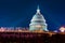 Marble dome of the United States Capitol building illuminated by rays of architectural light on a clear blue night with fountain