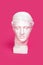 Marble head of young woman, ancient Greek goddess bust isolated on pink background