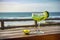 Margarita by the Shore. A Vibrant Classic Cocktail on a Wooden Table with a Serene Sea and Beach Background. Generative