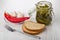 Marinated gherkins in open jar, fork, garlic, chili peppers in plate, fork on table