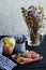 Marmalade on a pink saucer, next to apples, a blue glass with cherries, a checkered towel.