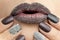 Maroon chocolate lips makeup with grains of white sand and multi-colored manicure