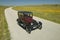 A maroon Model T driving down a scenic road surrounded by spring flowers off of Route 58, Shell Road, CA