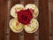 A maroon rose blooms on top of cream muffins on a wooden countertop on a Sunny summer day. Confectionery on display.