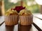 A maroon rose blooms on top of cream muffins on a wooden countertop on a Sunny summer day. Confectionery on display.