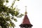 Maroon top of orthodox church bell tower with cross against sky and tree leaves