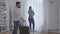 Married Caucasian couple standing indoors and looking at each other with anger. Young man holding travel bag, woman