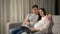 Married couple does online shopping for baby hugging on sofa