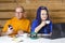 A married couple a man in glasses and a woman with blue afro braids at the table a woman drinks tea and works at a computer