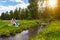 A married couple of men and women are sitting on the edge of a small stream at the edge of the forest near a forest during a picni