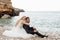 Married couple in wedding dress and official suit sitting on the coast of the sea or ocean near cliff rocks. Copy space