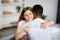 Married multiracial couple happy with positive result of pregnancy test, hugging each other at home