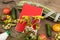 marrow squash, measure tape, blank red notepad, bottle of water, flowers, tomatoes and cucumbers on brown wooden table