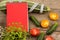 marrow squash, measure tape, blank red notepad, flowers, tomatoes and cucumbers on brown wooden table