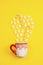 Marshmallows, sugar cubes and candy sticks in a holiday mug on a yellow background