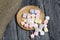 Marshmallows on a wooden plate. A little scattered nearby. On black pine planks