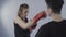 Martial art female theme. Sportswoman in red sports gloves practicing punches on paw held by personal Tekwando trainer