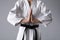 Martial arts master in keikogi with black belt on grey background, closeup