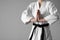 Martial arts master in keikogi with black belt on grey background, closeup. Space for text