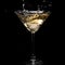 In a martini glass, vermouth ice falls, and splashes with drops on a black background