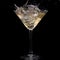 In a martini glass, vermouth ice falls, and splashes with drops on a black background