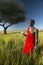 Masai Warrior near Acacia Tree listening to music on iPod by Apple in red surveying landscape of Lewa Conservancy, Kenya Africa