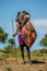 Masai warrior is standing in traditional clothing in a warrior`s headdress with spear and shield against the backdrop of savannah.