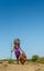 Masai warrior is standing in traditional clothing in a warrior`s headdress with spear and shield against the backdrop of savannah.