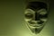 A mask that looks like a symbol of a group of hackers Anonymous. Tinted in olive color. Close-up. Shooting a subject in a dark key