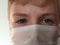 Masked child. The face of a 7-year-old boy in a protective white surgical mask close-up. Schoolboy with blond hair and blue-gray