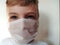 Masked child. The face of a 7-year-old boy in a protective white surgical mask close-up. Schoolboy with blond hair and blue-gray