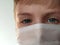 Masked child. The face of a 7-year-old boy in a protective white surgical mask close-up. Schoolboy with blond hair and blue-gray