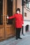 A masked and gloved doorman in a red coat and top hat opens the door.