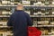 A masked man chooses wine in a supermarket. Large selection of alcohol on the shelves. Back view. Moscow, Russia, 09/15/2020