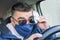 Masked man driving and wiping fogged glasses with a handkerchief because he cannot see while driving the vehicle road safety