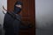 Masked thief with balaclava using crowbar to breaking into a house at night time. Crime concept.