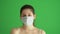 Masked woman protects himself from epidemic. Young female wearing medical mask at green screen. Close-up portrait at