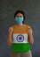 Masked woman wearing India flag color of shirt and standing with raised both fist on dark wall background