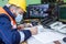 Masked worker wearing a helmet taking notes while sitting in front of the security screens