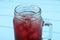 Mason jar of delicious iced hibiscus tea on light blue table, closeup