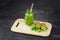 A mason jar filled with kiwi beverage, leaves of mint on a light wooden board on a dark stone background. Copy space.