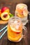 Mason jar glass of homemade peach iced water on a rustic wooden background.