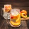 Mason jar glass of homemade peach iced water on a rustic wooden background.