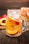 Mason jar glass of homemade peach iced water on a rustic wooden background.